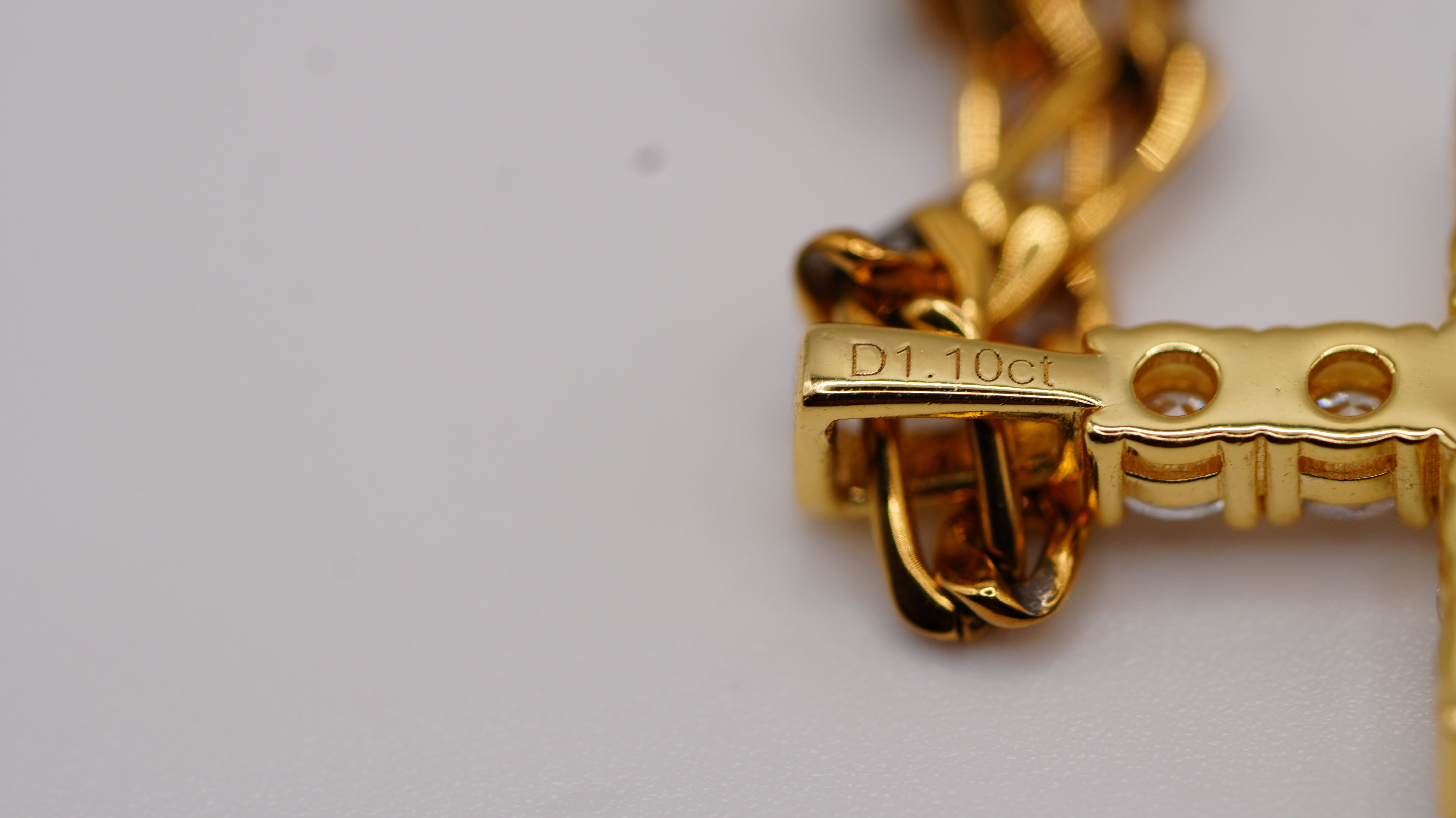 Close-up of a gold chain necklace with a cross pendant, showing a VVS D1 Clarity and 1.10 Carat hallmark stamp on the clasp against a plain light background.
