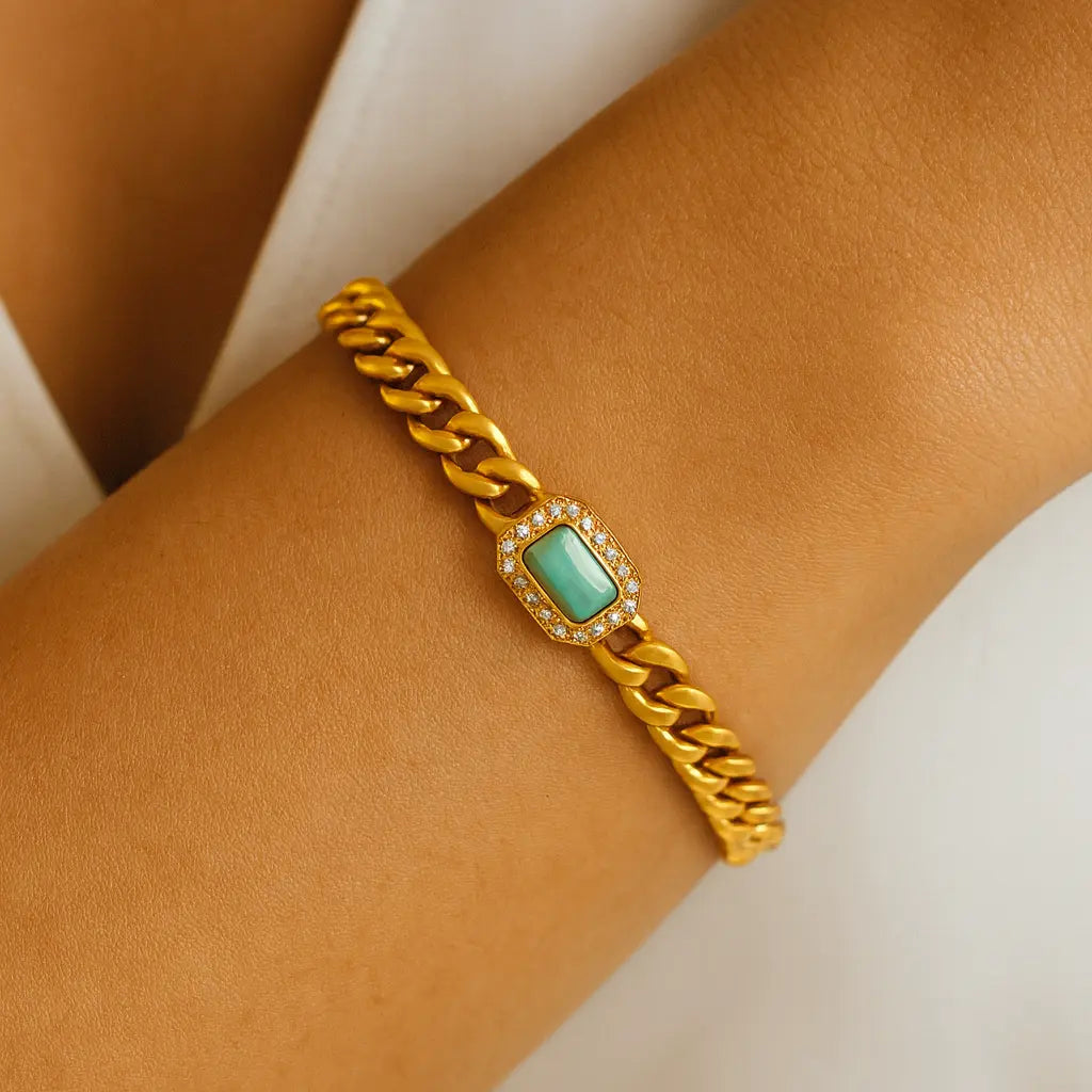 Gold chain bracelet with a green gemstone on a wrist against a white background