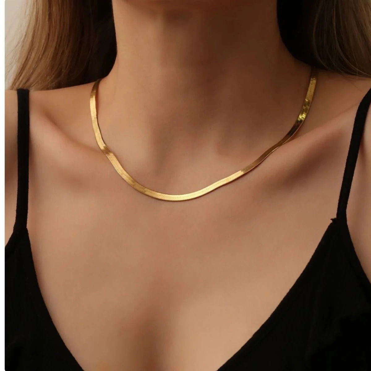Gold necklace on a person wearing a black top against a neutral background