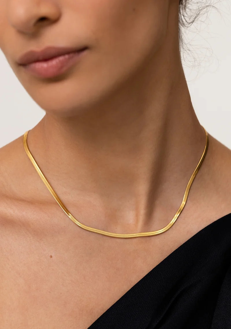 Gold necklace worn by a person against a neutral background