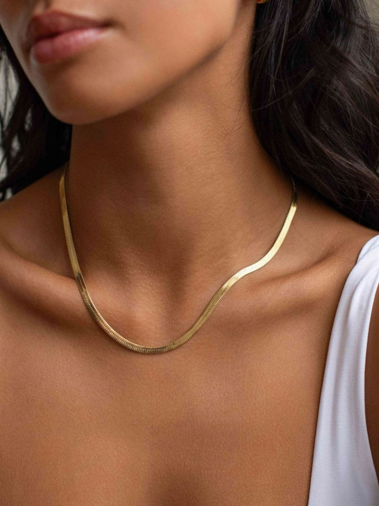 A close-up of a model wearing a thin, wavy gold chain necklace.